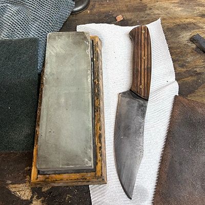 Knife with wooden handle and sharpening stone on a cloth.