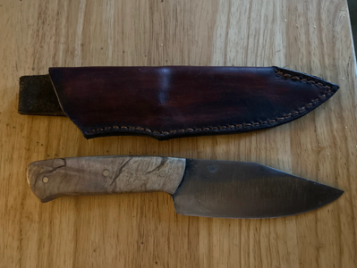 Fixed-blade knife with wooden handle and leather sheath on wooden surface.