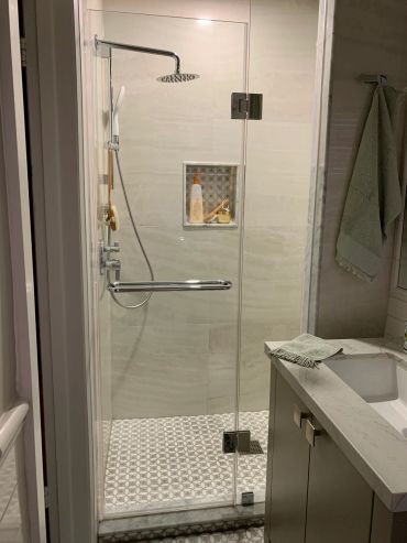 Modern bathroom shower with glass door and tiled floor.