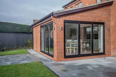 Modern brick house extension with large glass sliding doors overlooking a patio and garden.