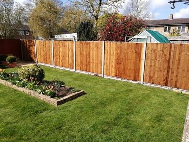 A tidy backyard with a wooden fence and a flower bed on a sunny day.