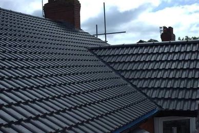 Newly installed dark gray roof tiles on residential houses under a cloudy sky.