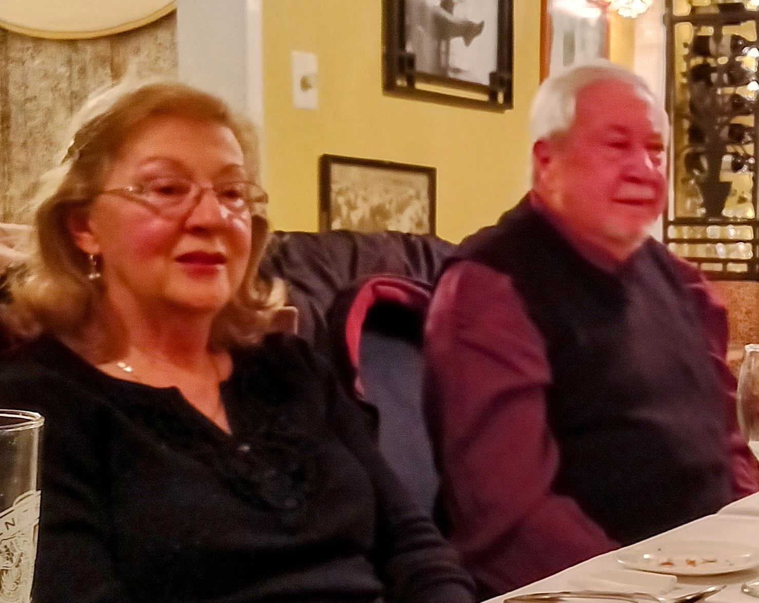 Elderly couple sitting at a dining table in a warmly lit room.