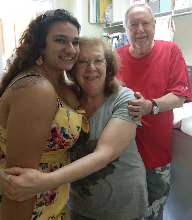 Three generations smiling and hugging in a cozy indoor setting.