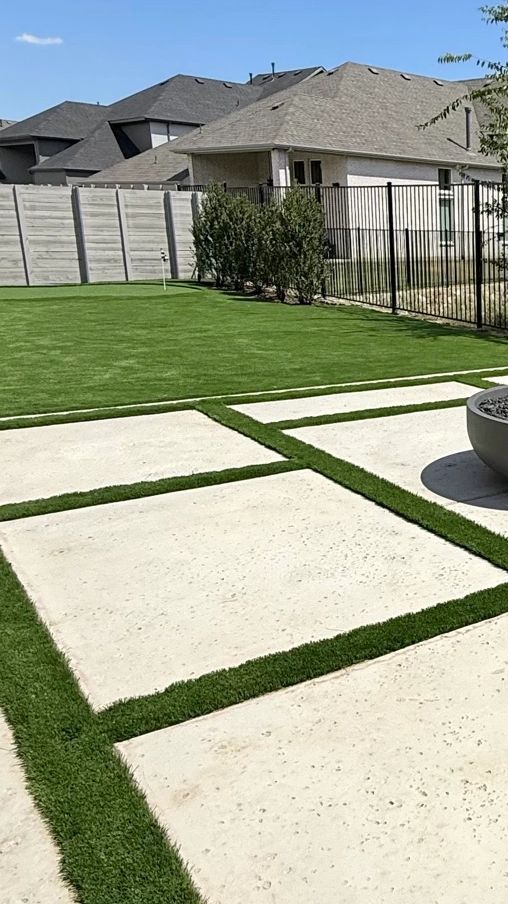 Residential backyard with artificial turf lawn, wooden privacy fence, and landscaped greenery — turf