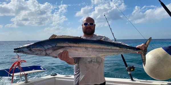 A happy customer holding a large Wahoo he caught on a Cozumel fishing charter.