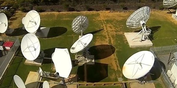 Satellite dishes in a fenced complex with surrounding greenery.