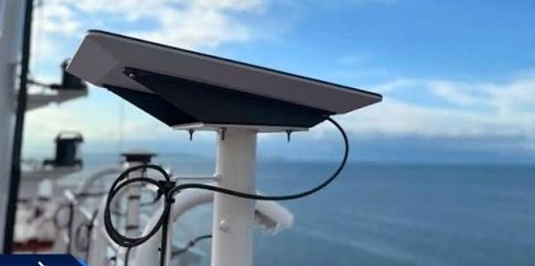 Solar panel mounted on a white pole near the sea.