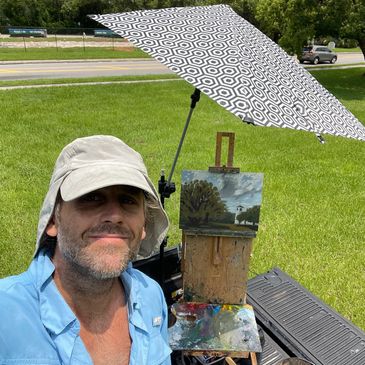 Man outdoor painting with umbrella for shade.