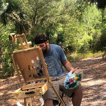 Man painting outdoors with easel and palette.