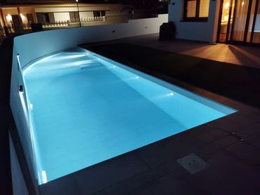 Piscina iluminada por la noche en un patio moderno.