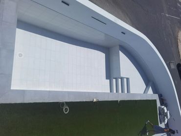 Piscina vacía con borde blanco y césped verde.