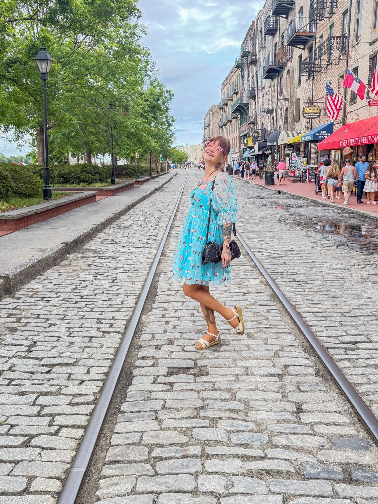 Woman in blue dress on cobblestone street with tram tracks.
