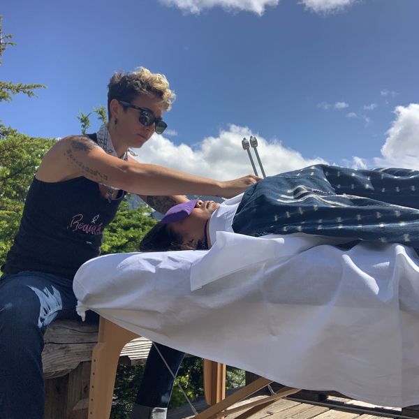 seated practitioner working on a client laying on a massage table using a tuning fork