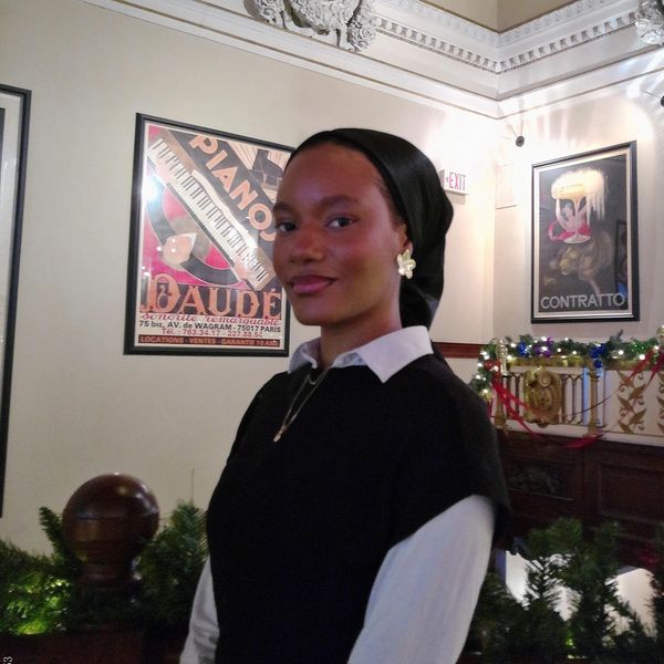 Woman wearing black headscarf and floral earrings in a decorated room.