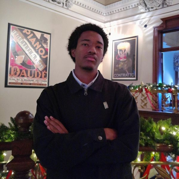 Man posing with arms crossed in a warmly decorated room with vintage posters.