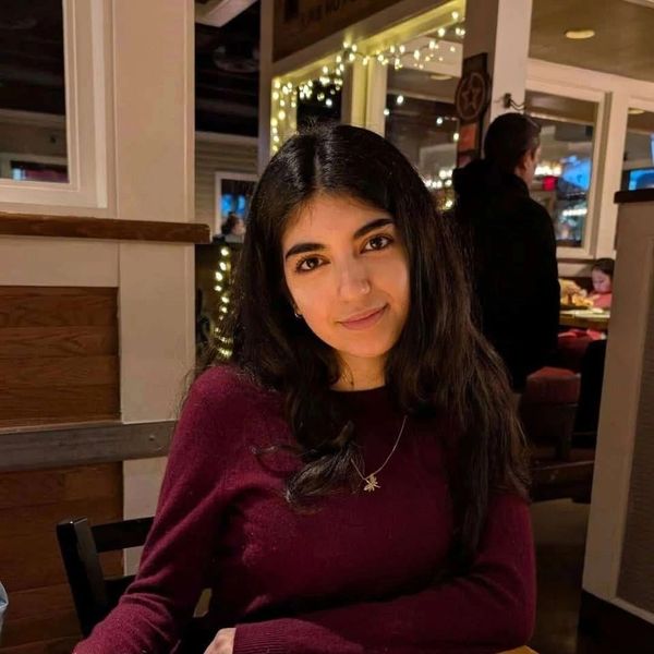 Young woman with long dark hair smiling indoors at a restaurant.