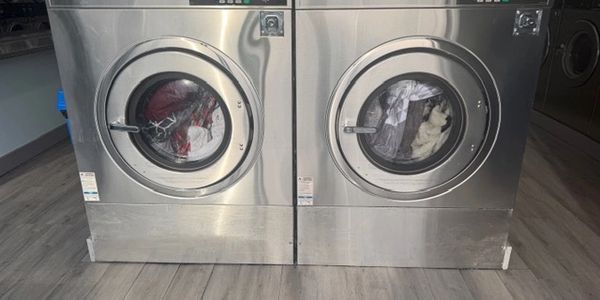 Two industrial Speed Queen washing machines in a laundromat with clothes inside.