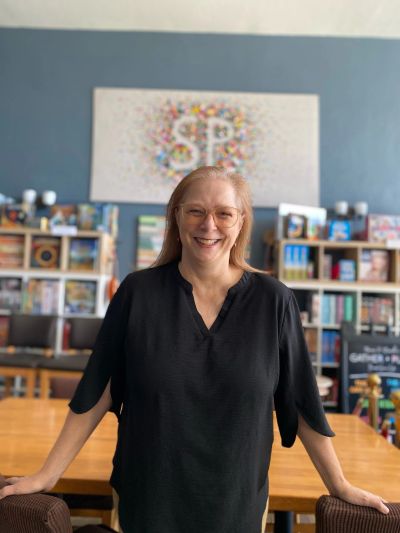 Smiling woman in a cozy room with books and games.