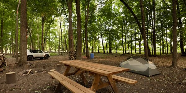 A campsite with a tent, picnic table, and parked car in a wooded area.