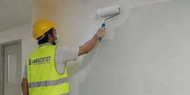 Man painting a wall white using a roller.