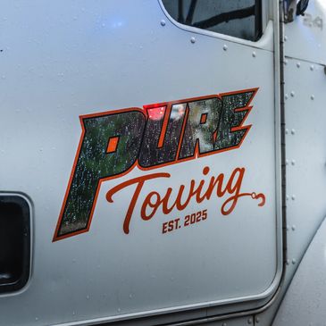 Close-up of a tow truck door with 'Pure Towing EST. 2025' logo and rain droplets.