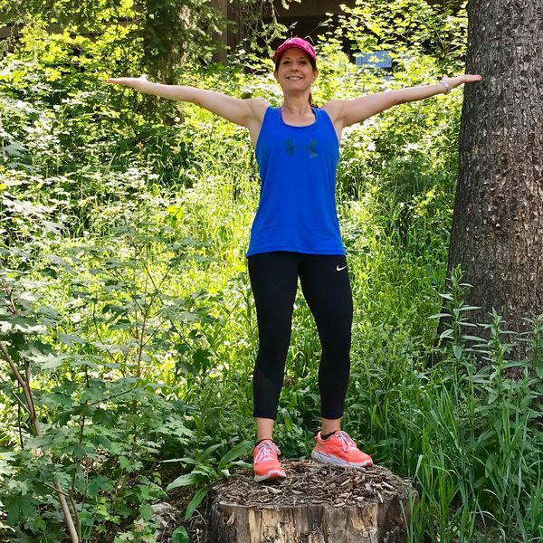 Jill on a tree stump with arms outstretched and smiling