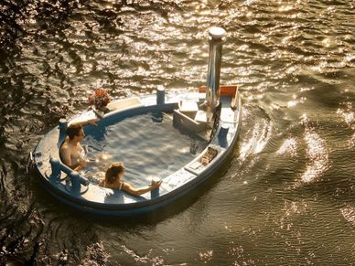 Two people relaxing in a floating hot tub on water at sunset.