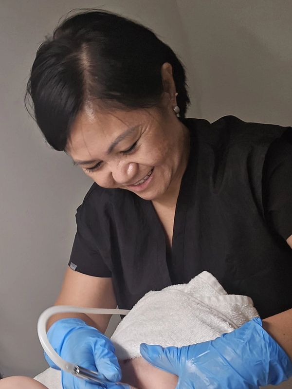 A woman wearing blue gloves performs a skincare treatment on a client's back.