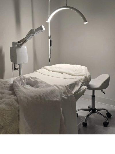 A clean, white spa or medical treatment room with a treatment bed and a stool.