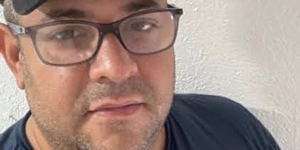 Man wearing glasses and a cap looking at the camera.