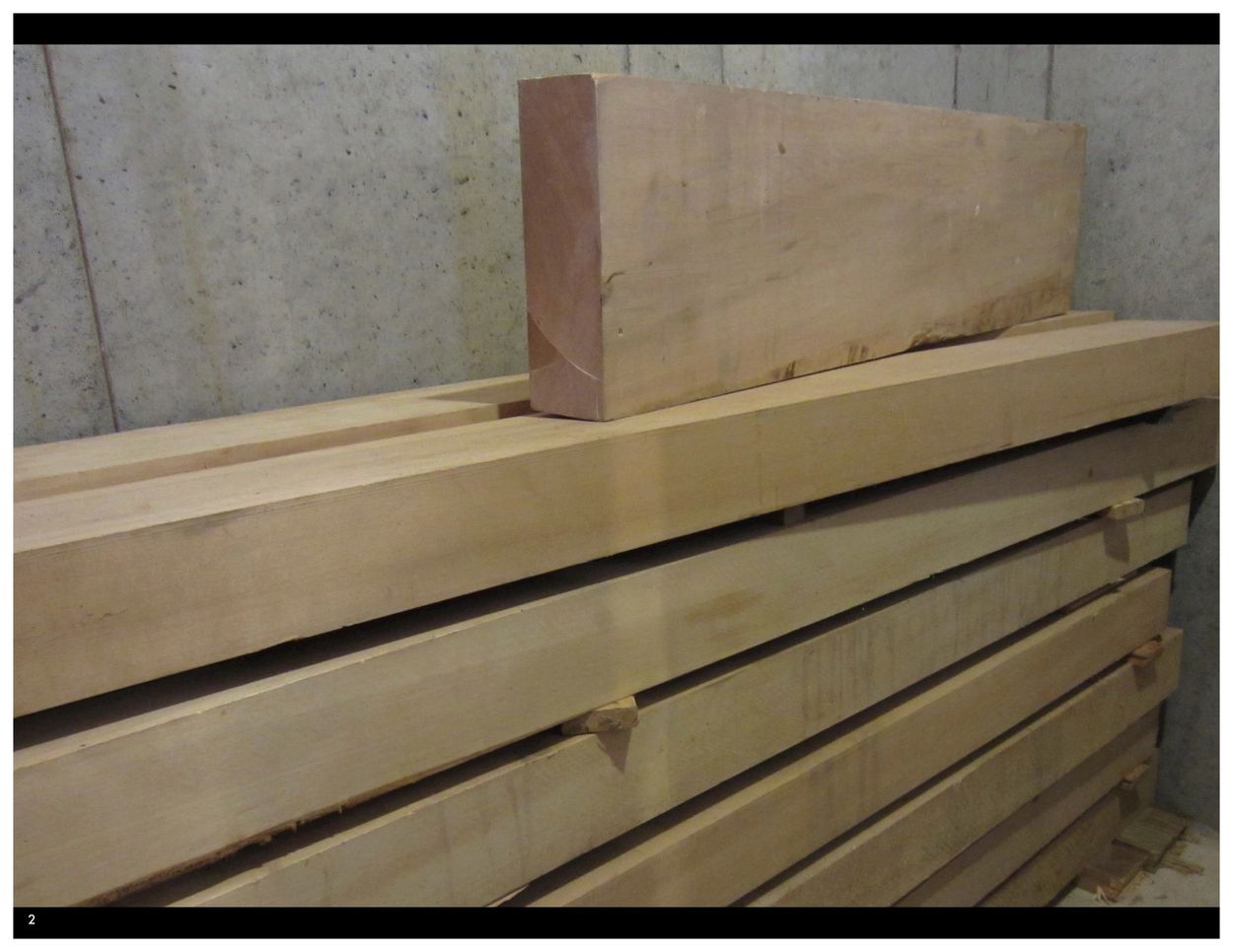 Stacked wooden beams stored against a concrete wall.