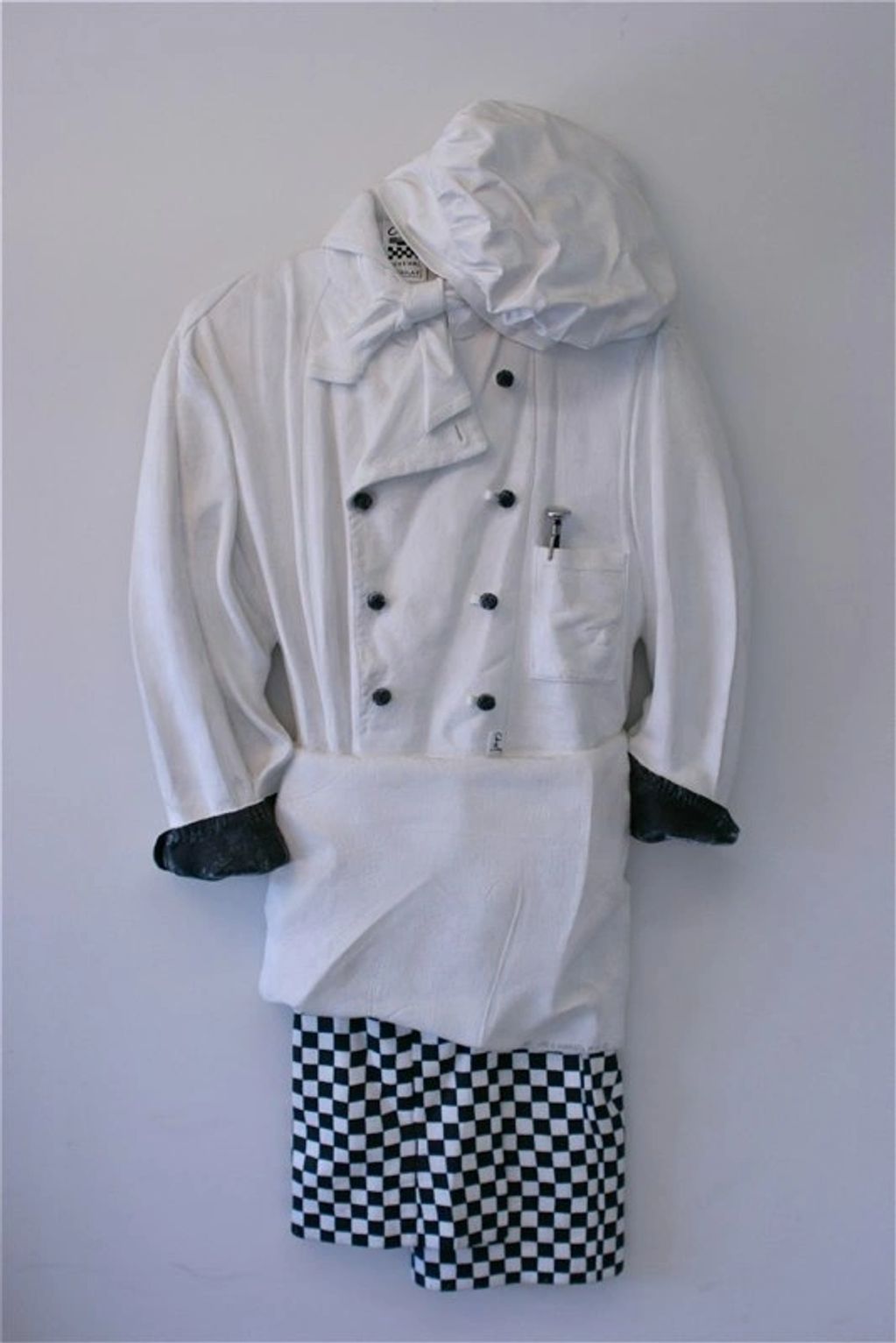 A chef's uniform with a hat and checkered pants hanging on a wall.