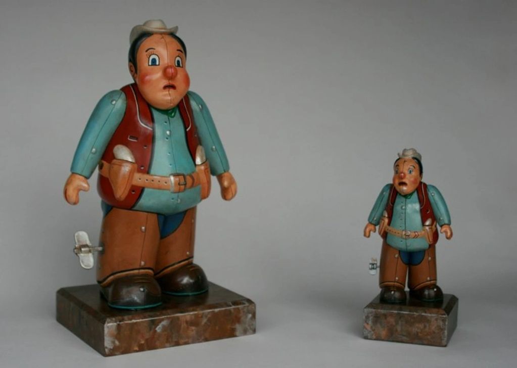 Two vintage wind-up cowboy toys on marble bases, one large and one small.
