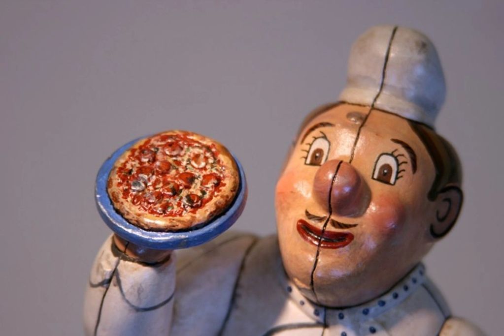 A ceramic chef figurine holding a miniature pizza on a blue plate.