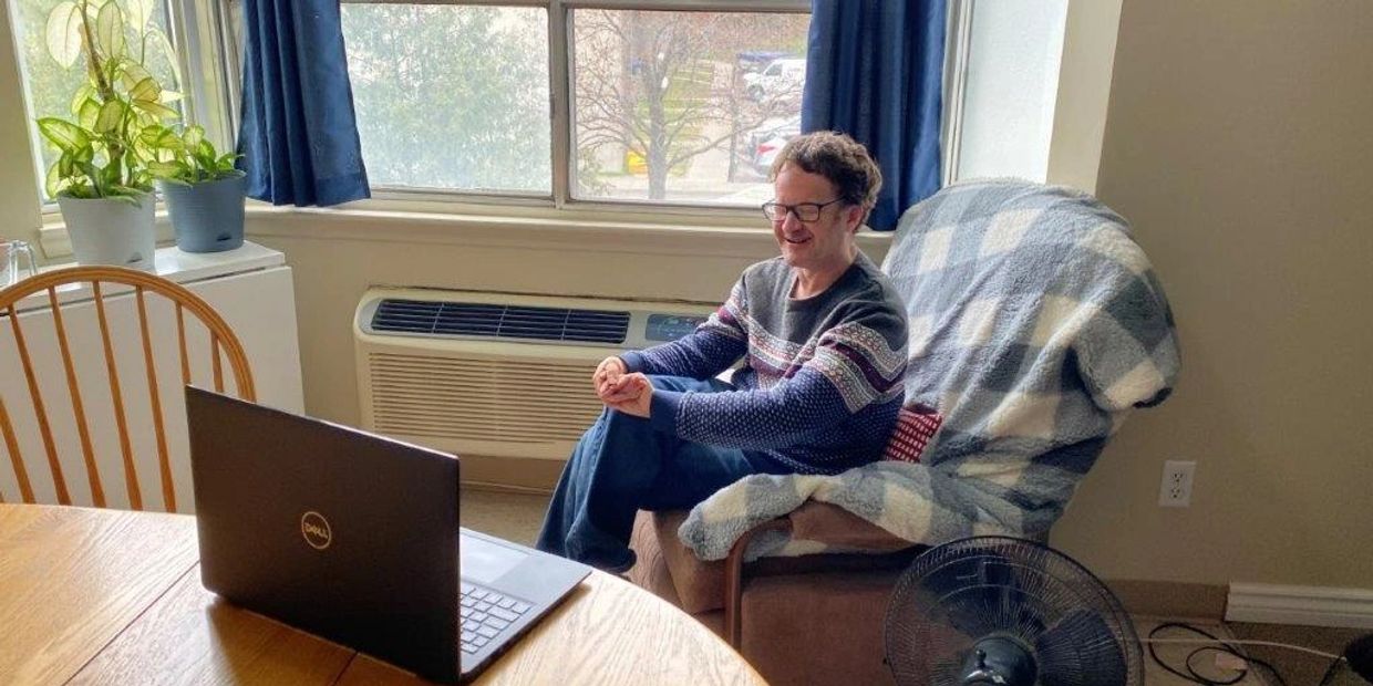 An SDS client sits on a recliner in a residential setting. He is on a Zoom call.