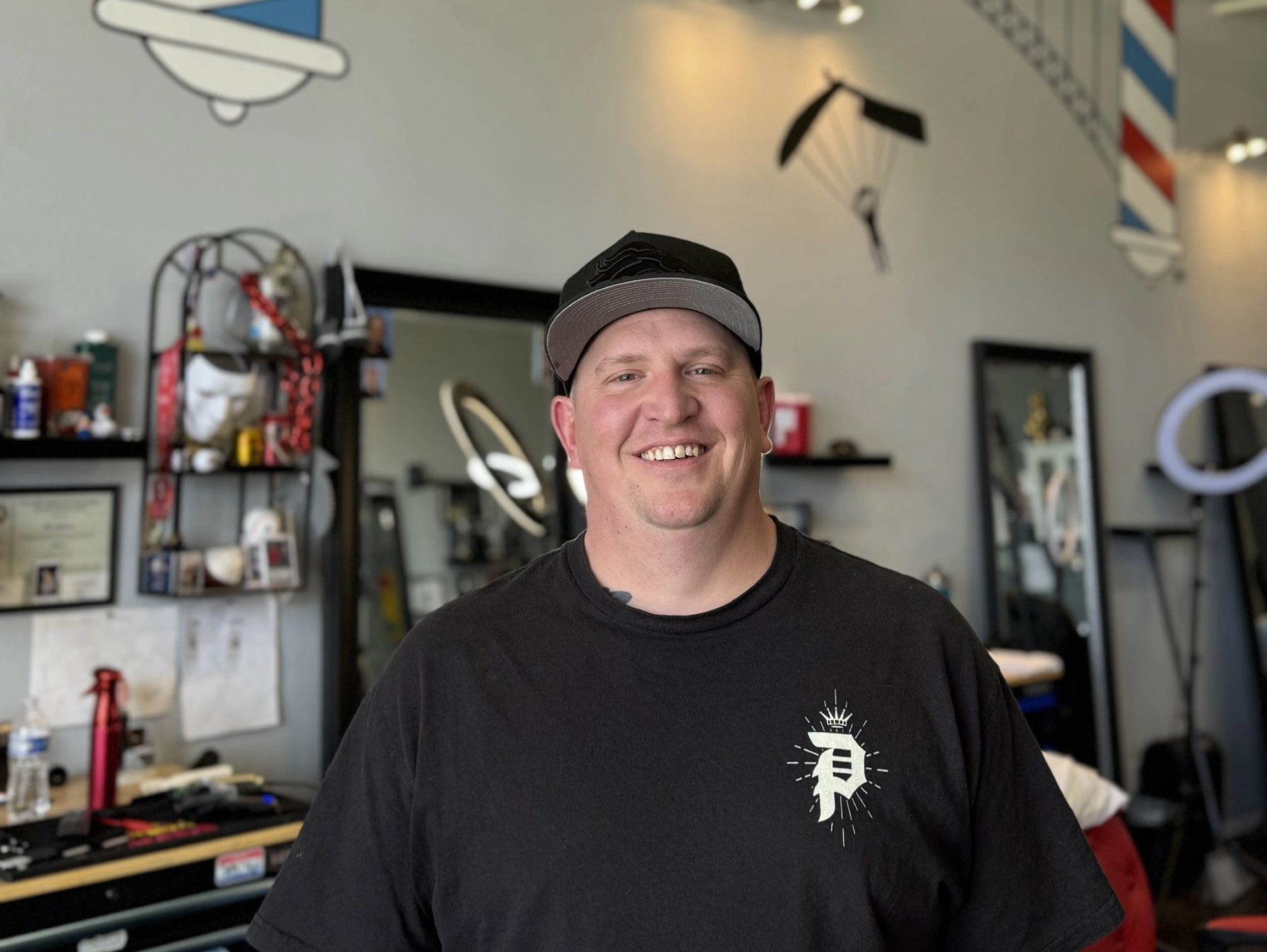 Smiling man wearing a black cap and t-shirt in a barber shop.