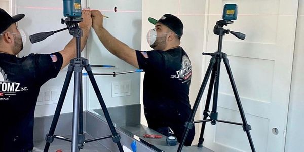 A man in a mask uses a laser level for precise measurements in a room.