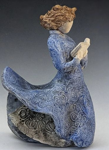 Sculpture of a woman in a flowing blue dress reading a book.