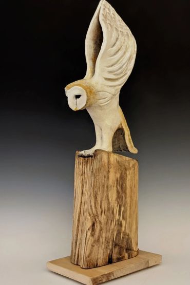 Wooden sculpture of an owl perched on a rustic wooden base.