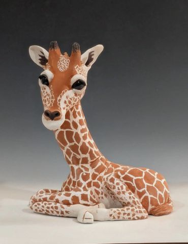A cute giraffe figurine lying down with big eyes.