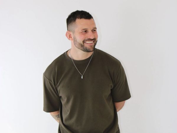 Smiling man in an olive green t-shirt standing against a white background.