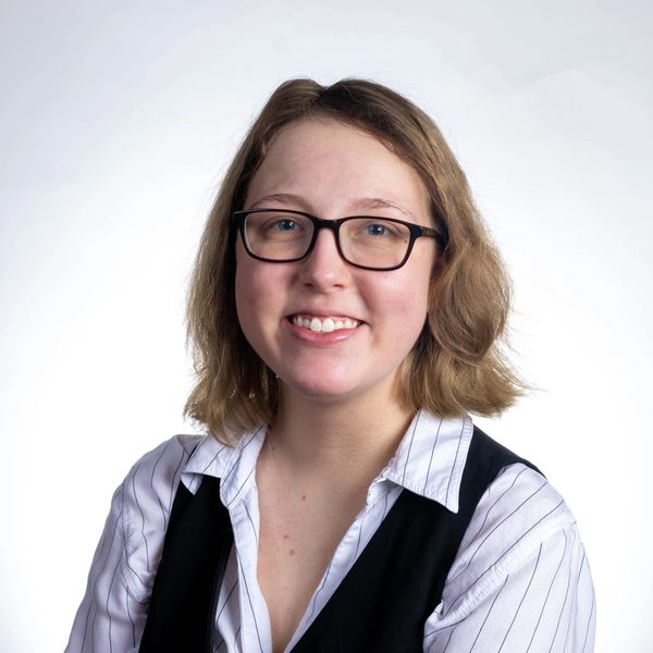 Smiling woman with glasses wearing a striped shirt and black vest.