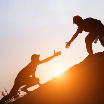 Two people helping each other climb a hill at sunset.