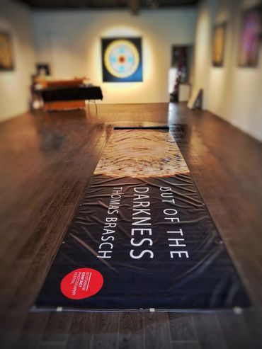 A vinyl banner of the show title lies stretched out on a gallery floor