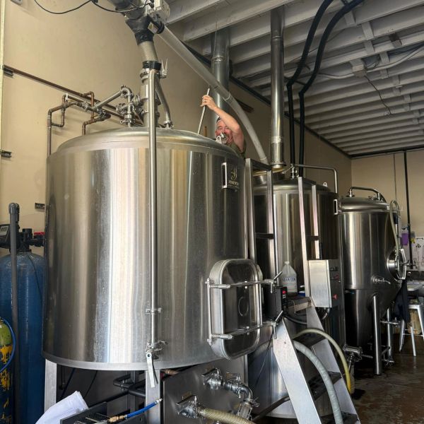 A person working on large stainless steel brew tanks.