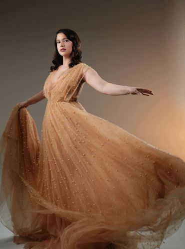 Woman in a flowing golden gown posing gracefully.