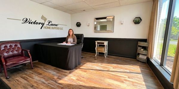 Woman sitting at a desk in a modern office with Victory Lane Home Buyers sign.