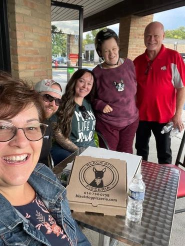 Smiling customers gather around an outside table for a picture.  