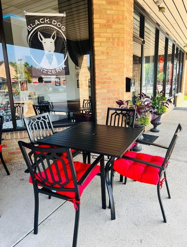 Outdoor dining area with two tables and four chairs each with red cushions. 